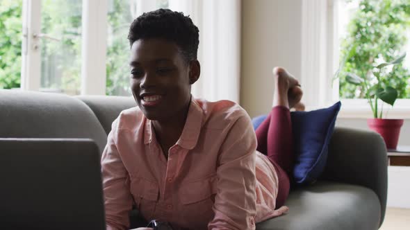 African american woman using laptop while lying on the couch at home