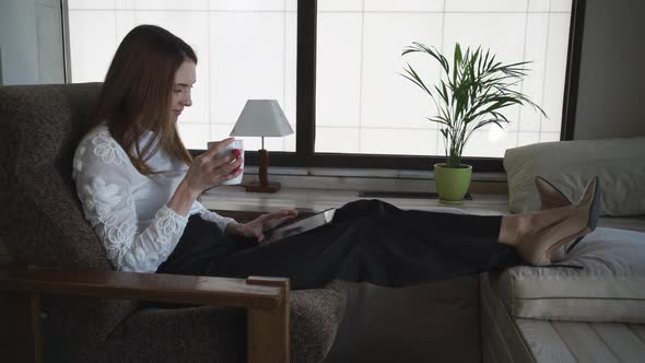 The Woman Sitting and Drinking Coffee Is Looking Through Her Device