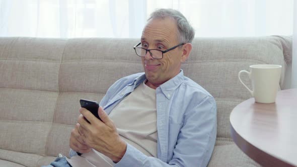 Elderly Man Rejoices Looking Into Smartphone