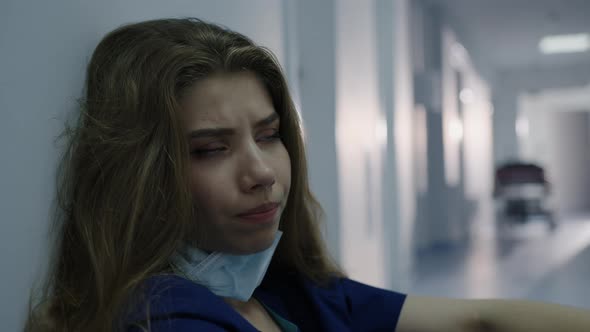 Doctor Removes a Mask From Her Face While Sitting on the Floor of the Hospital