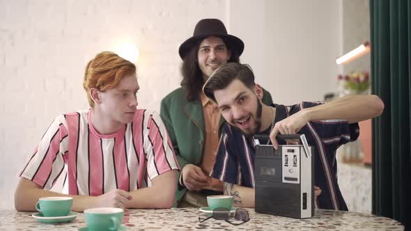 Smiling Man Winking Turning on Retro Tape Recorder and Group of Cheerful Male Friends Dancing