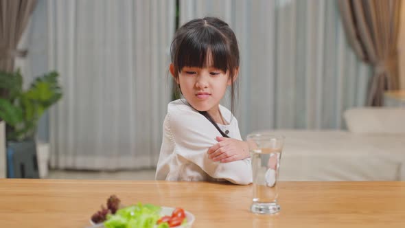 Unhappy Asian little young girl child don't want to eat green vegetables on dinner plate.