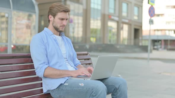 Young Man with Wrist Pain Using Laptop While Sitting on Bench