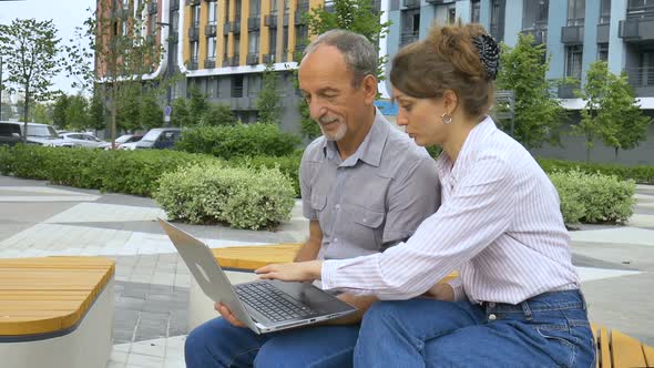 Young Employee is Teaching Her Older Colleague How to Use Laptop and Corporate Software Sitting on