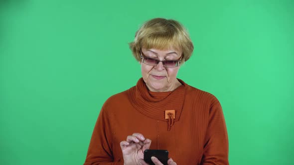 Portrait of Senior Woman Is Texting on Her Phone isolated Over Green Background