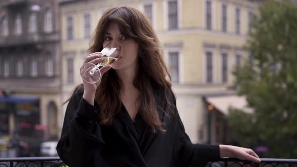 Brunette Woman Drinking a Glass of Champagne on a Balcony in Budapest