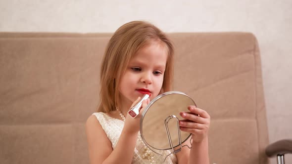 Young Blonde Girl Holds a Mirror and Paints Her Lips with Rich Red Lipstick