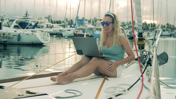 Young Woman Communicates Via Laptop While Sitting on a Yacht. Video Chatting, Video Call Concept.