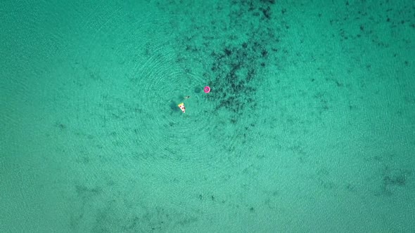 High aerial view of two young girls swimming and playing in sea with inflatables.