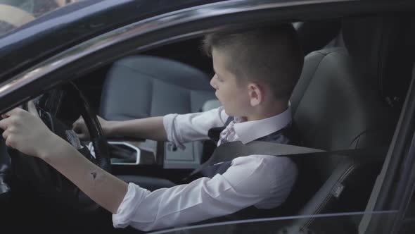 The Young Well-dressed Boy Learning To Drive the Car Sitting at the Drivers Seat