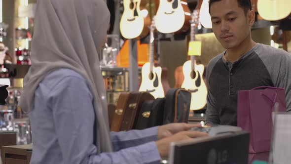 An upwardly mobile Asian Muslim man using a mobile phone - smartwatch to pay for a product at a sale