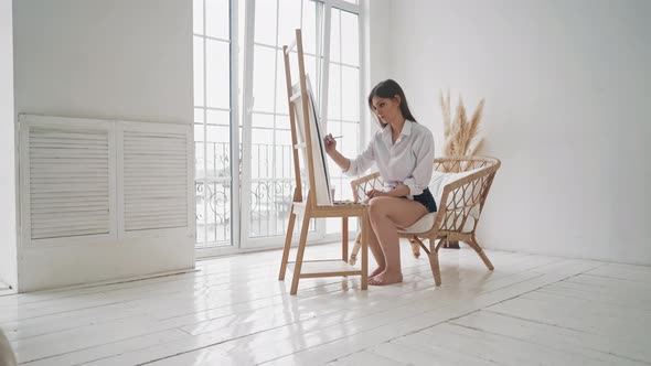 Attractive Woman Draws Painting on Wooden Easel in Studio