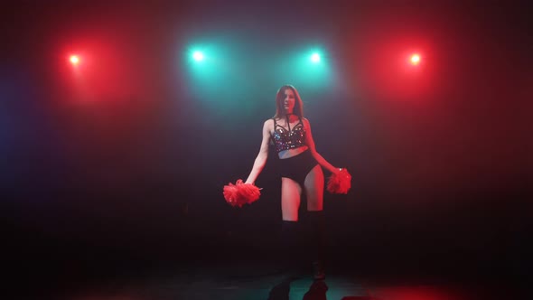 Silhouette of Slender Cheerleader Dancing with Pompoms Against a Background of Smoke and Bright Blue