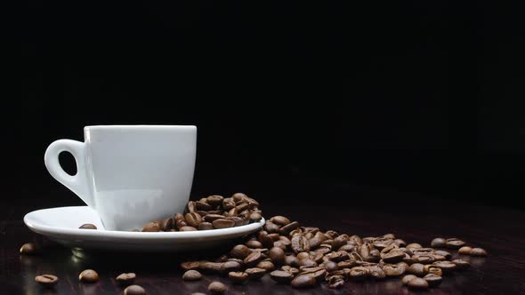 A Cup of Hot Coffee with Roasted Beans Around on a Black Background in  Resolution in Slow Motion