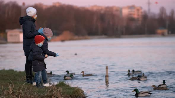 Mother, son and daughter in medical masks feed ducks in the Park on the lake.