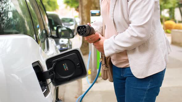 Woman charging electric car at charging station 4k