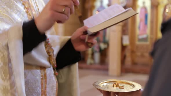 A Priest in the Church During the Wedding Ceremony Consecrates Gold Wedding Rings for the Bride alt