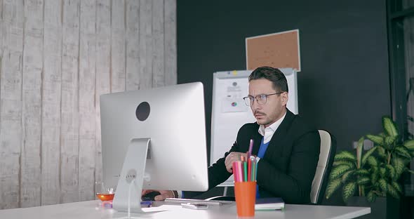 Businessman in Glasses Sits at Computer in Office