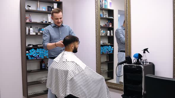 Young Man in Barber Shop Sits in an Armchair. Barber Cuts His Hair with a Trimer