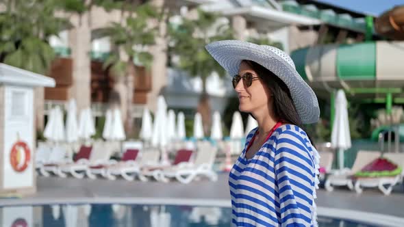 Smiling Relaxed Travel Girl in Sunglasses and Hat Walking at Luxury Resort Area Enjoying Vacation