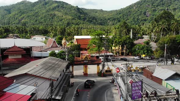 Cars Riding Along Road Near Temple Gates. Vehicles Riding Along Asphalt Road Through Small Town Near