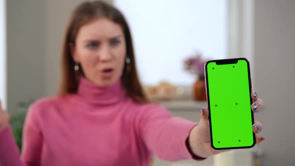 Smartphone with Green Screen and Blurred Surprised Caucasian Woman Gesturing Saying Wow at