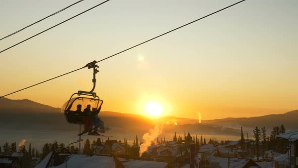 Tourist Silhouettes Move on Ski Lift Over Buildings Roofs