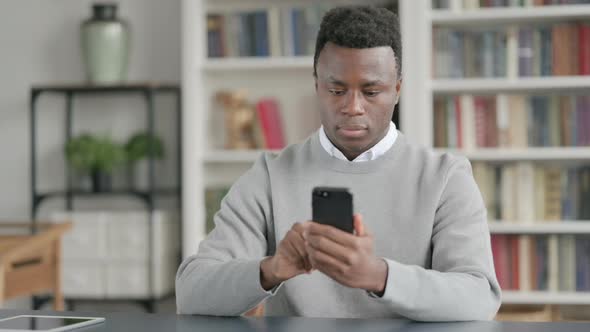 Attractive African Man Using Smartphone in Library