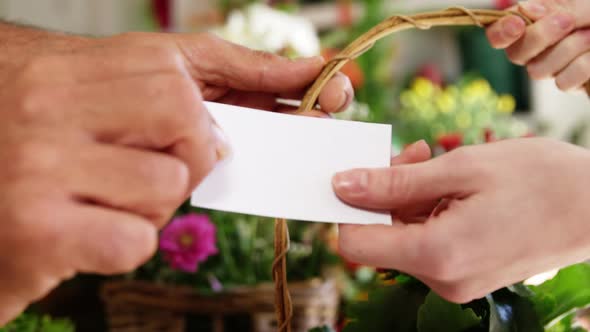 Florist giving visiting card and flower basket to customer in flower shop