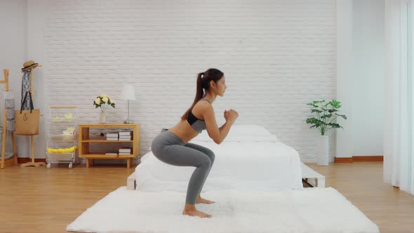 Athletic Healthy Asian woman in sportswear workout squats excercise at home in bedroom