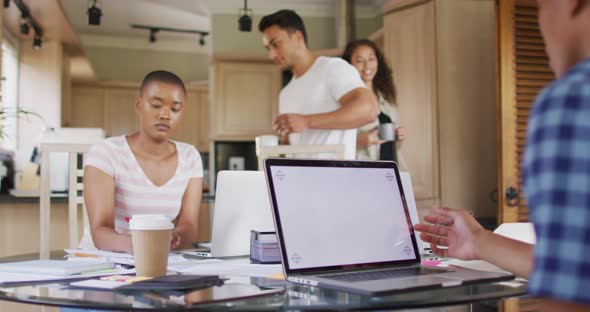 Group of diverse male and female friends working in kitchen on laptops with copy space