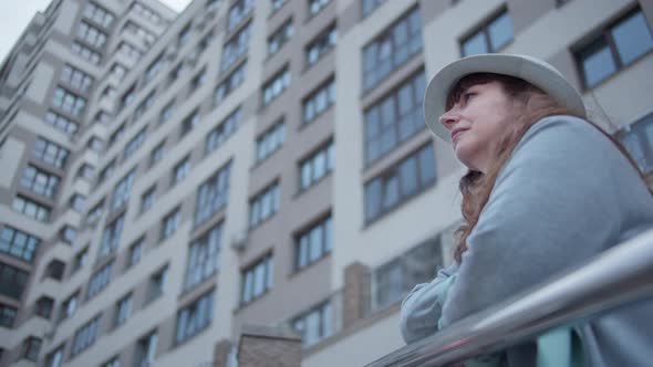 Traveler Brunette Woman in a Hat Stands on the Street at the Top and Looks Around