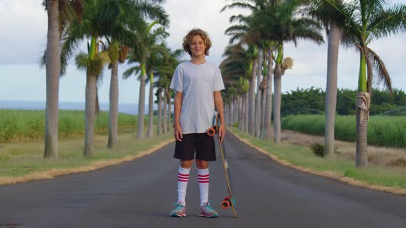 A Teenager with Long Hair Rides a Skateboard Along a Beautiful Road with Palm Trees