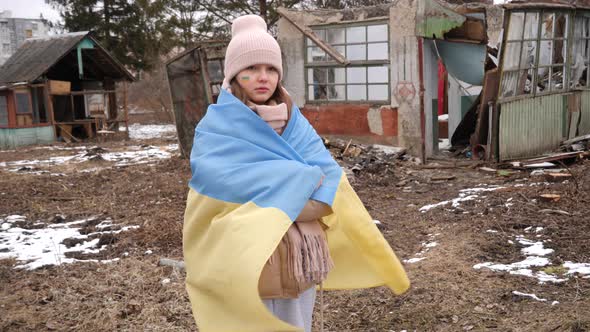 A girl wearing in the Ukrainian flag stands sad against the background of destroyed houses. War in U alt