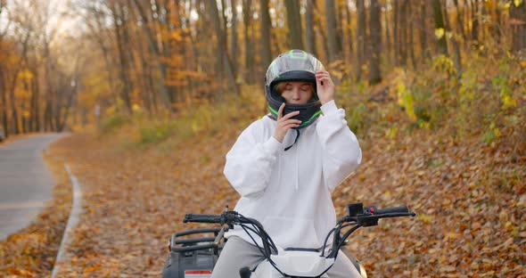 Blonde Girl in a White Sweatshirt Sitting on an ATV in the Autumn Forest