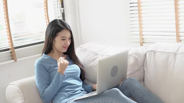 Young asian woman working online laptop with smile and happy sitting on couch.