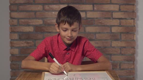 Child Sitting at the Desk Holding Flipchart with Lettering Signature on the Background Red Brick