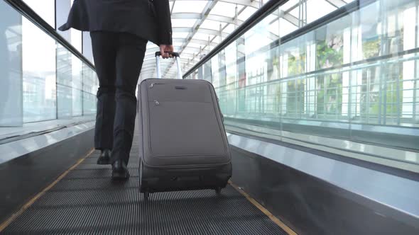 Legs of Successful Businessman Running in Hall of Terminal and Pulling Suitcase on Wheels. Camera