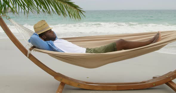 Side view of African american man sleeping in a hammock on the beach 4k