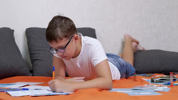 Child Writing with a Pen in a Notebook Lying on an Orange Bedspread in Room