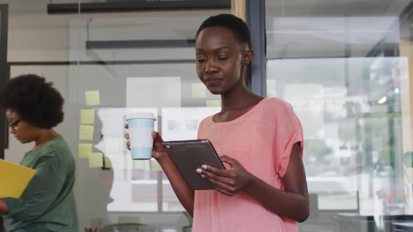 African american businesswoman drinking takeaway coffee using tablet and smiling to camera in office