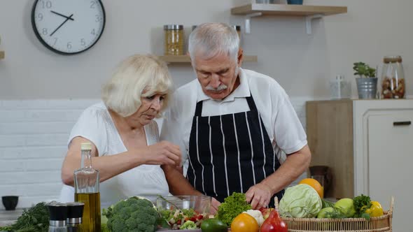 Senior Grandparents in Kitchen Interior. Senior Woman and Man Cooking Salad with Fresh Vegetables