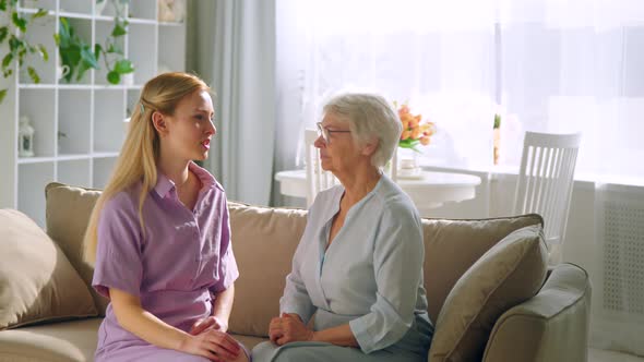 A young girl and an elderly woman are talking on the couch in a bright room
