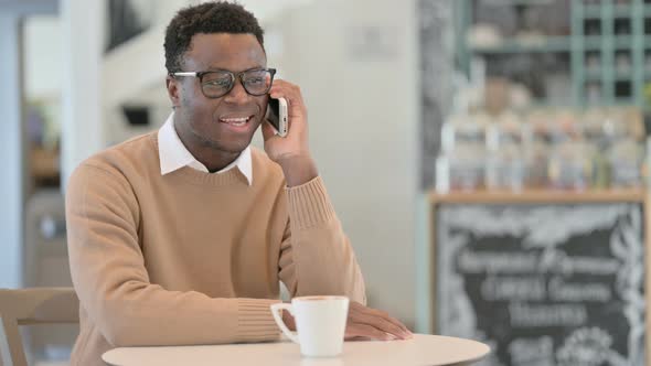 African American Man Talking on Phone While Drinking Coffee in Cafe