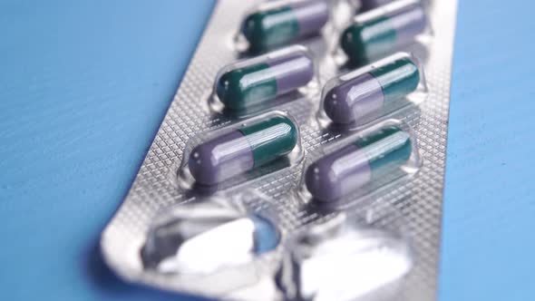 Blister pack of green purple medical capsules on a blue wooden table.