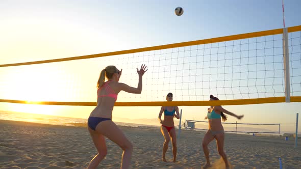 Women players play beach volleyball and a player hitting spiking the ball.