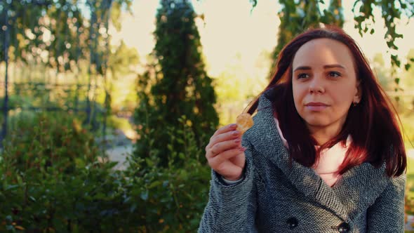 Portrait of a Beautiful Woman Who is Sitting in the Park on a Sunny Autumn Day Eating Potato Chips