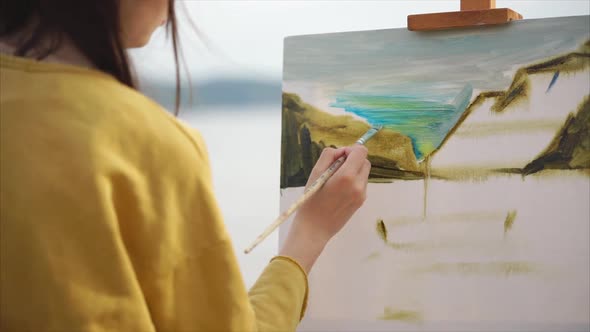 Woman Artist Paints an Oil Painting on Canvas Which Stands on an Easel