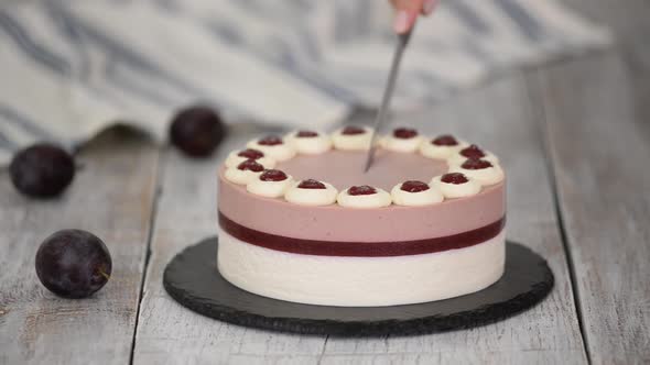 Cutting delicious plum mousse cake with whipped cream.