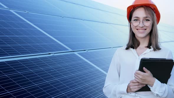 Beautiful young engineer standing near solar panels outdoors, Green Energy Concept